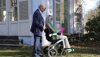 Man pushing woman in wheelchair outdoors near house